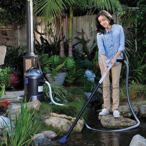 Person cleaning a pond with a vacuum hose in a garden setting